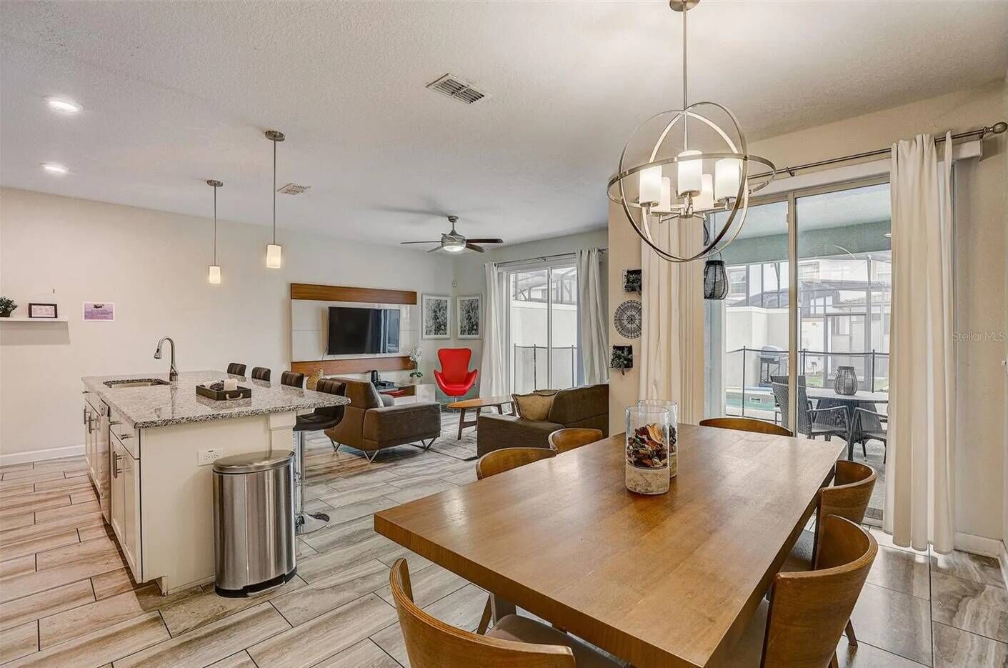 Cozinha moderna com ilha central, área de refeições com mesa de madeira e sala de estar com uma cadeira vermelha.