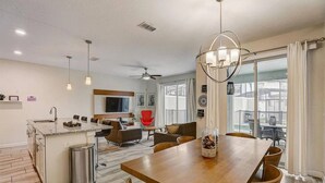 A modern kitchen with a central island, dining area with a wooden table, and a living room with a red chair.