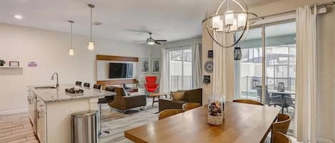 Cocina moderna con una isla central, zona de comedor con una mesa de madera y sala de estar con una silla roja.