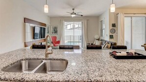 A modern kitchen with granite countertops, a stainless steel sink, and a ceiling fan.
