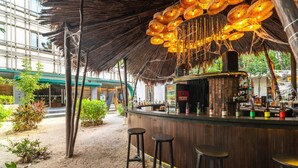 Una zona de bar con techo de paja, barra de madera y taburetes.