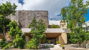 Un edificio moderno con una fachada geométrica original, rodeado de abundante vegetación y un patio de grava.