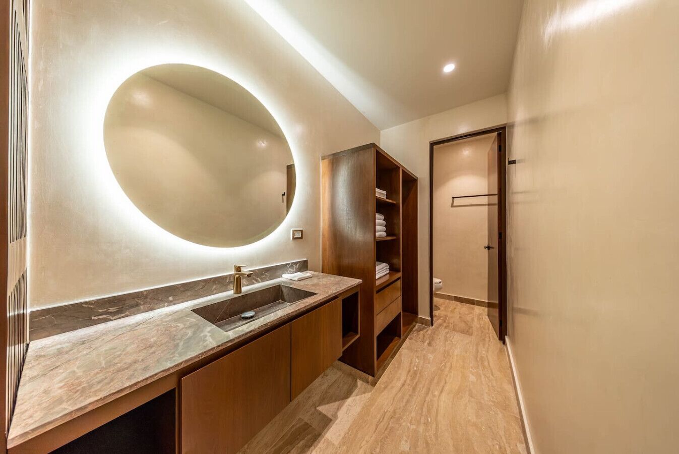 A modern bathroom with a marble countertop, a round mirror, and a wooden vanity.
