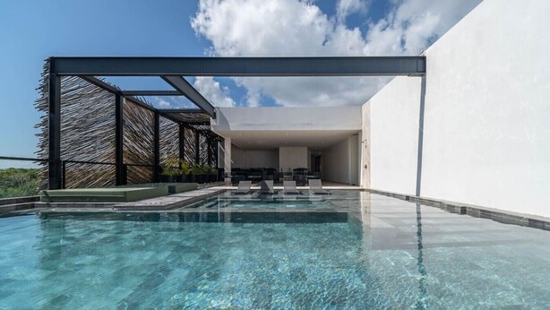 Una piscina moderna al aire libre con agua cristalina, rodeada por una estructura minimalista y una pared blanca.