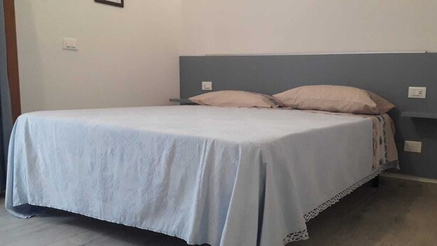 Een eenpersoonskamer met een grijs hoofdbord, wit beddengoed en een eenvoudig, schoon design.