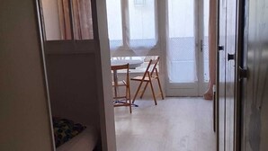 A room with a bunk bed, a small table with chairs, and a large window with curtains. - 
500 m beach studio cabin in residence Cap Atlantic, St Palais/mer swimming pool (Saint-Palais-sur-Mer)