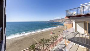 Een hotel aan het strand met een balkon dat uitkijkt over de oceaan, een pier en een zandstrand.
