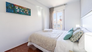 Een hotelkamer met een bed, een schilderij aan de muur, een raam met gordijnen en uitzicht op een balkon.