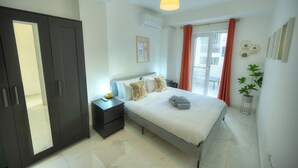 Quarto com cama, mesas de cabeceira, guarda-roupa e janela com cortinas.