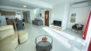 Uma sala de estar moderna com sofá, mesa de centro de vidro, TV e área de jantar com mesa e cadeiras.