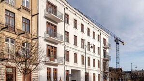 A multi-story building with a white facade, balconies, and a construction crane in the background.