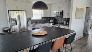 Eine moderne Küche mit Edelstahlgeräten, einem dunklen Holztisch und einer großen Pendelleuchte.