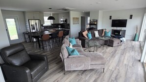 Ein geräumiger Wohnbereich mit einem Ledersofa, einem grauen Couchsofa und einem Glastisch. Im Hintergrund ist eine Küche mit modernen Geräten zu sehen.