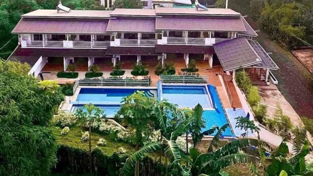 Un grand immeuble à plusieurs étages, doté d’une piscine et entouré d’une végétation luxuriante.