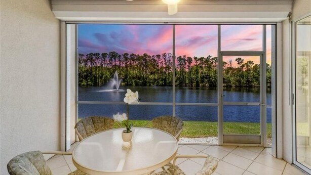 A room with a large sliding glass door leading to a lake view, a round table with chairs, and a ceiling fan. - Spacious 3-bedroom first floor coach home with attached garage in North Naples (Naples)