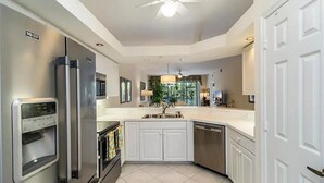 A modern kitchen with stainless steel appliances, white cabinetry, and a large island. - Spacious 3-bedroom first floor coach home with attached garage in North Naples (Naples)