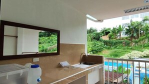 A modern bathroom with a large mirror, a sink, and a toilet. There is a small trash bin and a storage container on the counter. The bathroom has a view of a pool and greenery outside. - Tropical Comfort & Charm (Puerto Princesa)