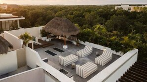 Terraza en la azotea con techo de paja, mobiliario exterior y vistas a un follaje denso.