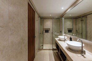 Un baño moderno con cabina de ducha de vidrio, dos lavamanos y un espejo grande.