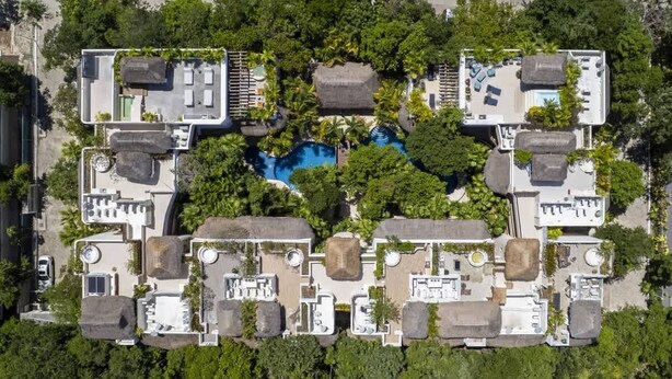 Vista aérea de un resort con varias edificaciones, una piscina central y follaje circundante.