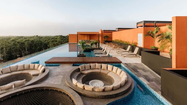 Piscina infinita no terraço com espreguiçadeiras, um espaço de estar circular e vista para a paisagem ao redor.