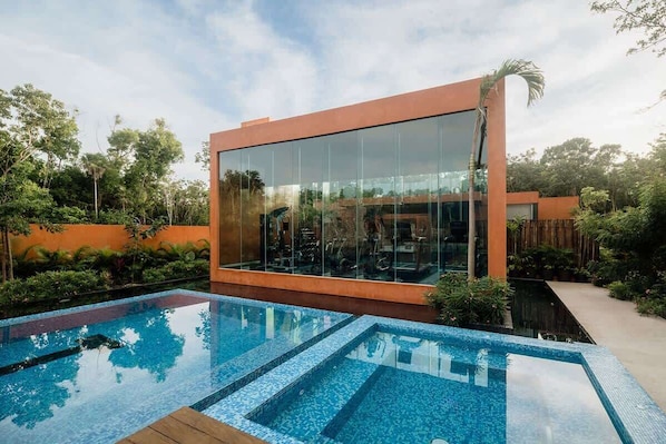 A modern building with large glass windows, a swimming pool, and lush greenery.