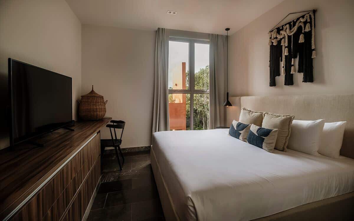 A hotel room with a bed, a television, a small table, and a window with curtains.