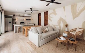 A modern living space with a sofa, coffee table, and chairs, a kitchen area with a refrigerator and microwave, and a ceiling fan.