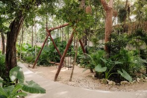 A garden with a swing set, trees, and various plants.