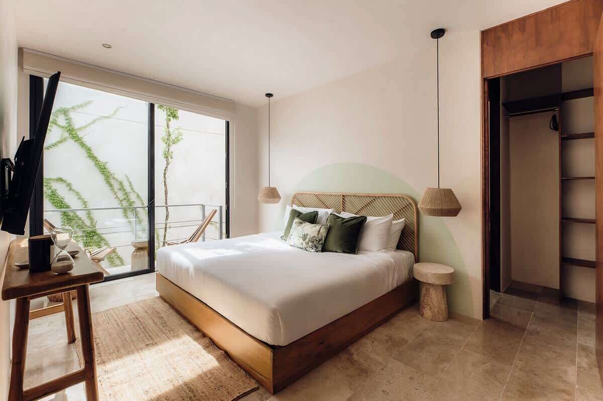 A bedroom with a bed, bedside tables, a wardrobe, and a view of greenery outside.