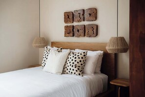 Ein Bett mit weißer Bettwäsche und Kissen mit Punkten, ein Holz-Kopfteil und zwei an der Wand befestigte Lampen.