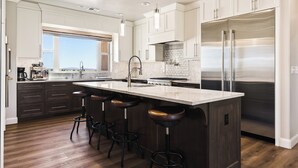 A modern kitchen with a large island, stainless steel appliances, and dark wood flooring.