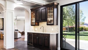 A modern kitchen with dark cabinetry, a stainless steel sink, and a view of a landscaped backyard through glass doors.