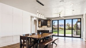 A spacious dining area with a wooden table and benches, a kitchen with dark cabinets, and a large sliding glass door leading to a patio with a view of mountains.