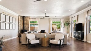 A spacious living room with a sectional sofa, two armchairs, a wooden coffee table, and a flat-screen TV on a black cabinet.