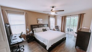 Un dormitorio con una cama grande, un escritorio, una silla, un ventilador de techo y vistas al exterior.