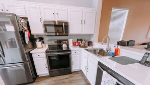 Una cocina moderna con armarios blancos, electrodomésticos de acero inoxidable, horno empotrado, microondas y un lavamanos.