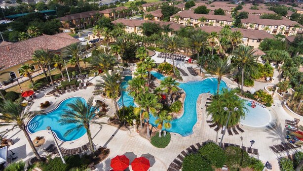 Un resort con varias piscinas, palmeras y vistas de edificios residenciales circundantes.
