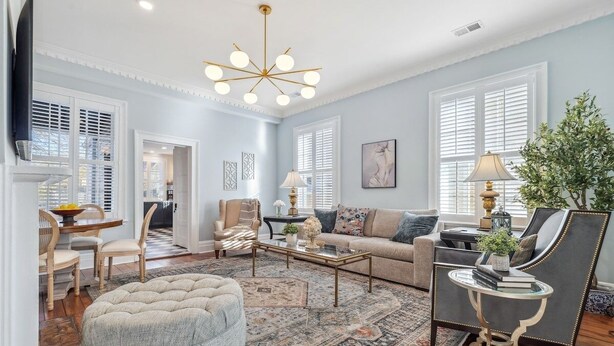 A spacious living room with a large sofa, a coffee table, and a tufted ottoman. There is a chandelier, a television, and a plant in the room. - Palazzo Sul Monte-Due (Wilmington)