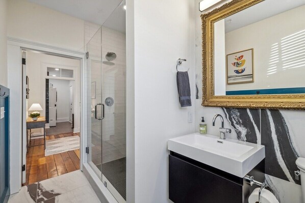 A modern bathroom with a glass shower enclosure, a white sink, and a large mirror with a decorative frame.