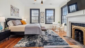 Un dormitorio con cama, chimenea y dos ventanas con persianas.