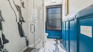 Un baño con baldosas de mármol, cabina de ducha de vidrio, inodoro y muebles en azul.