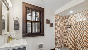 A bathroom with a white sink, a mirror, a window with blinds, and a shower with patterned tiles. - Palazzo Sul Monte-Cinque (Wilmington)