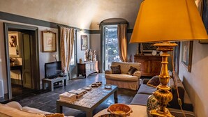 A cozy living room with a sofa, armchair, coffee table, and a lamp. There is a television and a cabinet with decorative items. - Modica Luxury with Terrace (Modica)