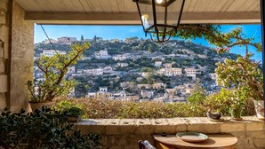 A terrace with a view of a hillside village, a wooden table, and potted plants. - Modica Luxury with Terrace (Modica)
