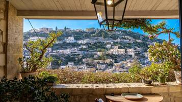 A terrace with a view of a hillside village, a wooden table, and potted plants.