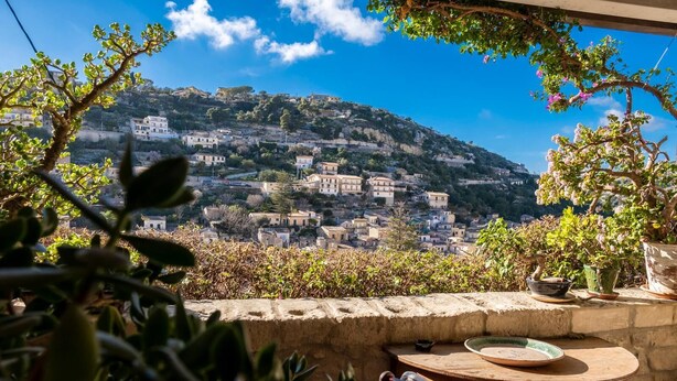A terrace with a view of a hillside town, stone walls, and potted plants. - Modica Luxury with Terrace (Modica)