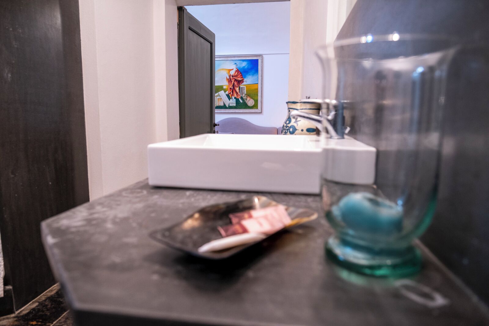 Une salle de bain avec un lavabo blanc, un miroir et un flacon de savon pour les mains posé sur un comptoir foncé.