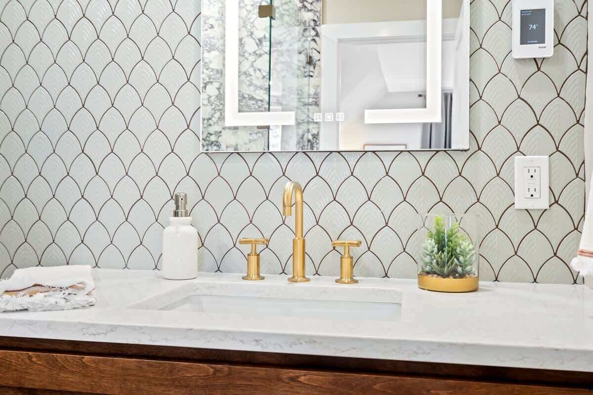 A bathroom with a marble sink, gold faucets, and a mirror.