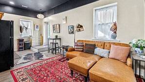 Uma sala de estar moderna com um sofá de couro, um tapete estampado em vermelho e uma área de jantar com mesa e cadeiras.